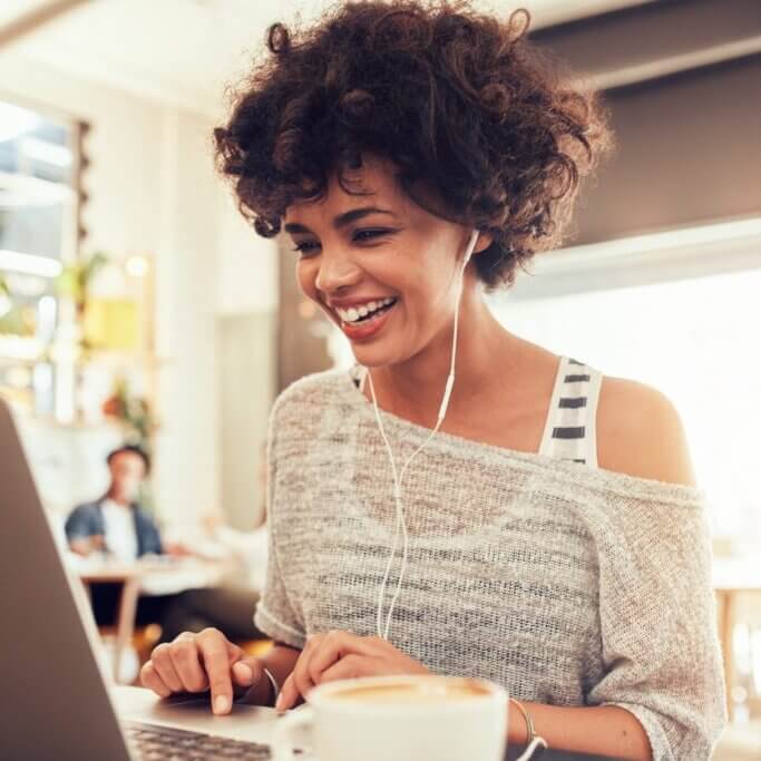 Image of happy woman using laptop while sitting at cafe. Young african american woman sitting in a coffee shop and working on laptop.